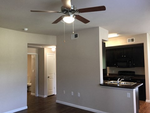 an empty living room with a ceiling fan and a kitchen