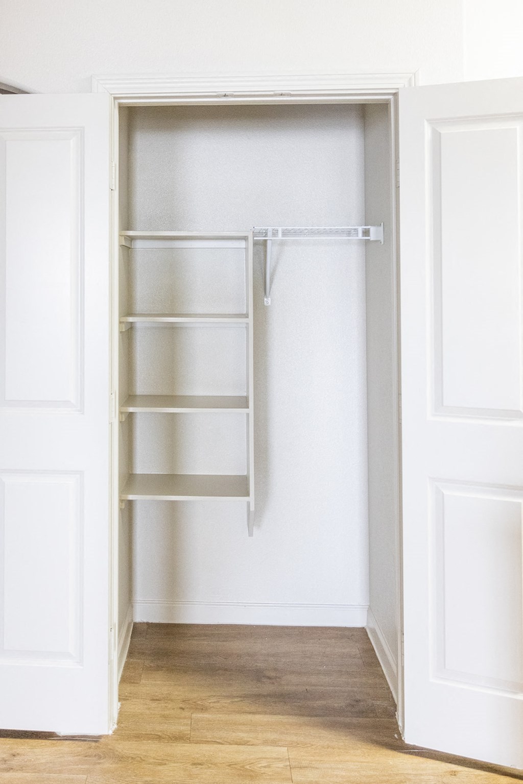 a white closet with empty shelves and a wood floor
