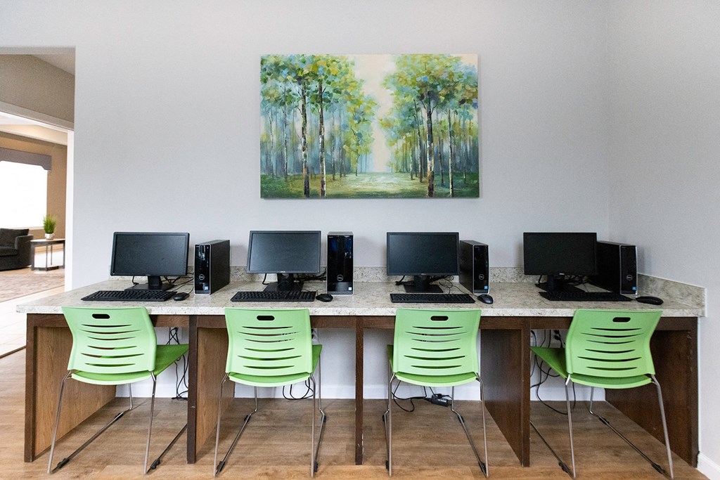 a long desk with computers and a painting on the wall