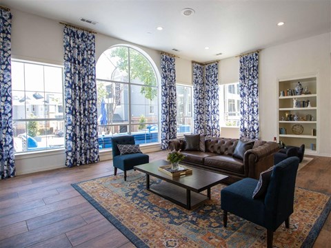 A living room with a brown leather couch, a blue chair, and a coffee table with a vase of flowers on it.