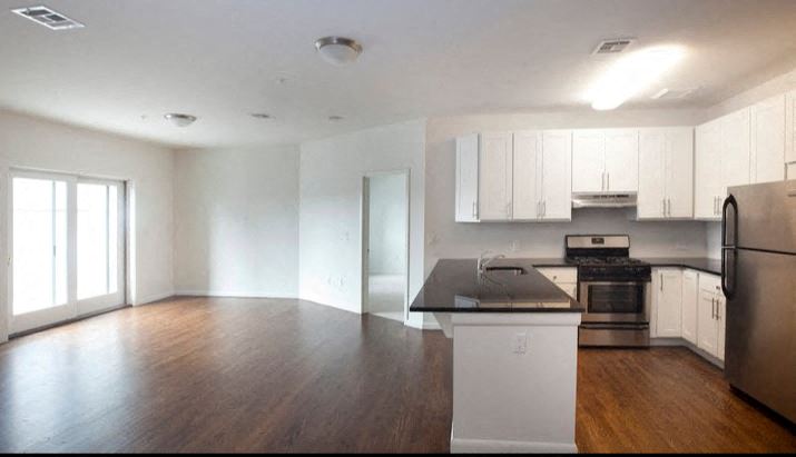 Open layout living room and kitchen with hardwood floors, black granite counter tops, white cabinets and stainless steel appliances