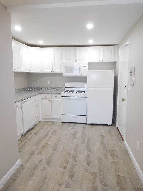 Renovated kitchen with granite counters, white cabinets and white appliances