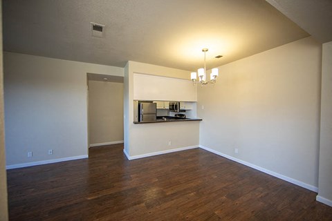 an empty living room with a kitchen in the corner