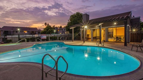 A swimming pool in a backyard with lights on.