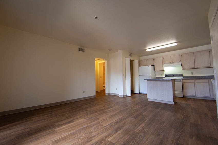 an empty living room and kitchen with wood floors