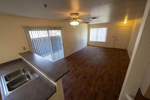an empty living room with a kitchen and a ceiling fan