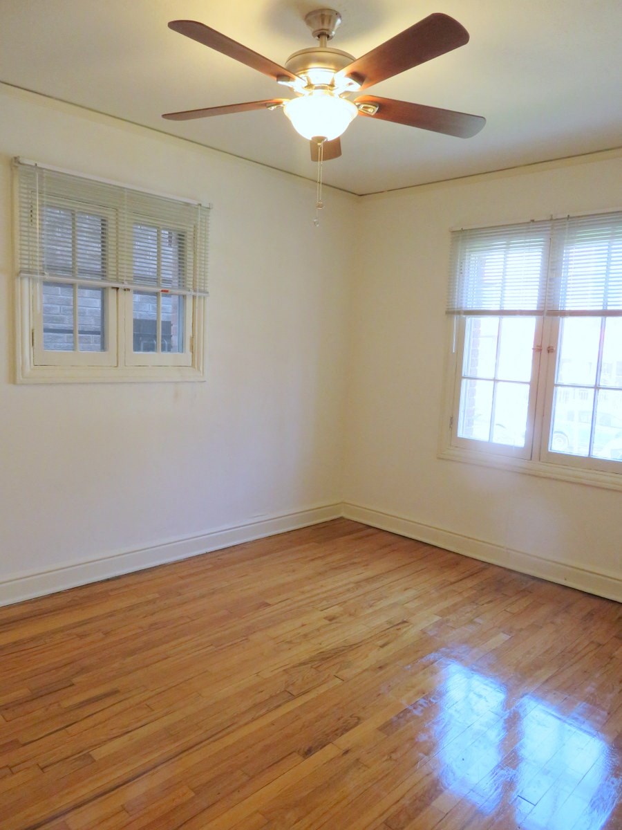 an empty room with a ceiling fan and two windows