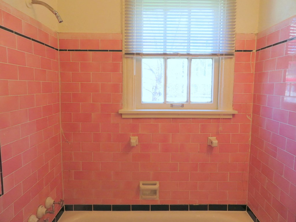 a pink tiled bathroom with a window and a tub