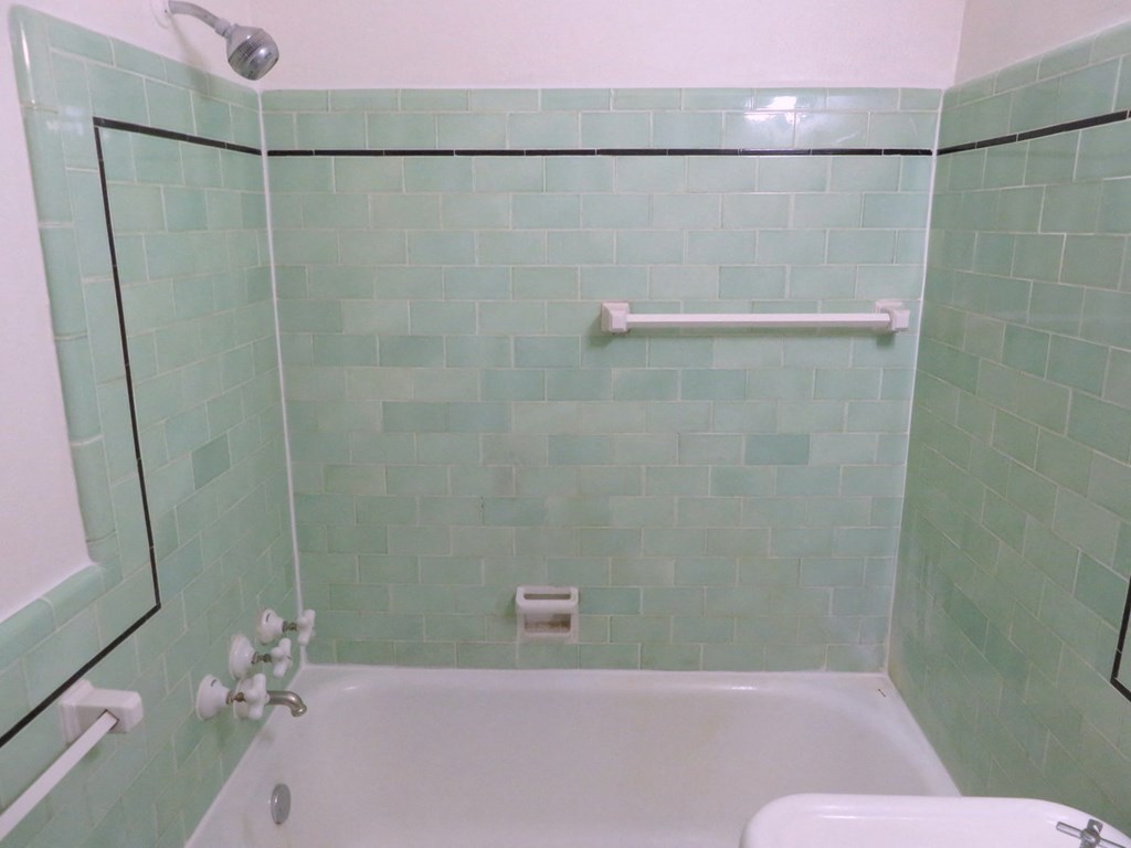 the bathroom has a shower and a tub with green tile