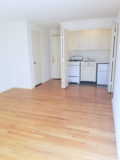 an empty kitchen with white appliances and a wooden floor