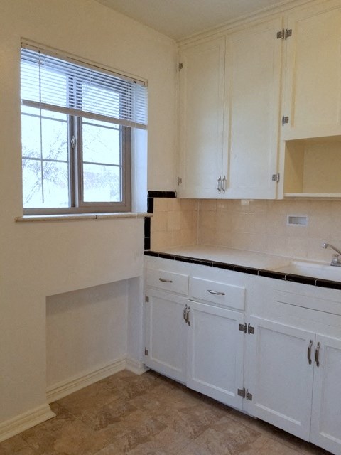 an empty kitchen with white cabinets and a window