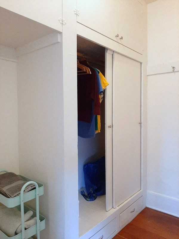 a white closet with a door open and some clothes in it