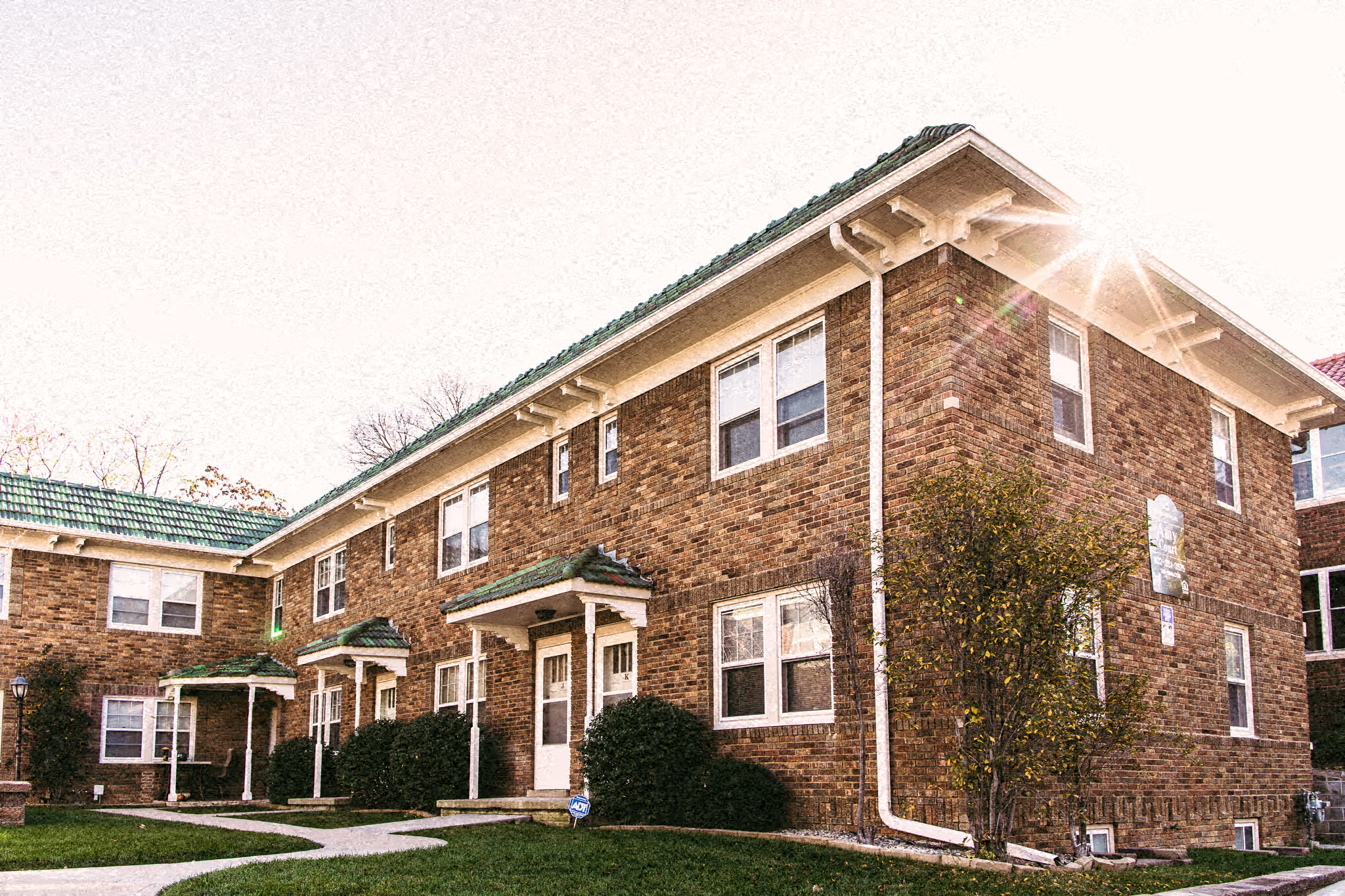 the front of a brick apartment building with the sun shining through the window