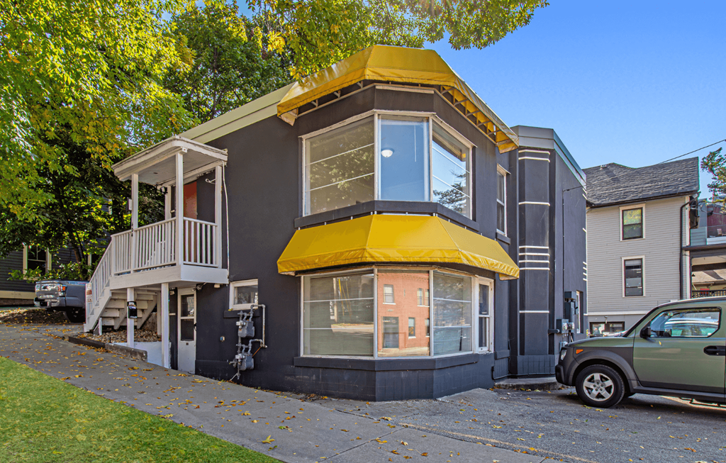 a small house with a yellow roof on the corner of a street