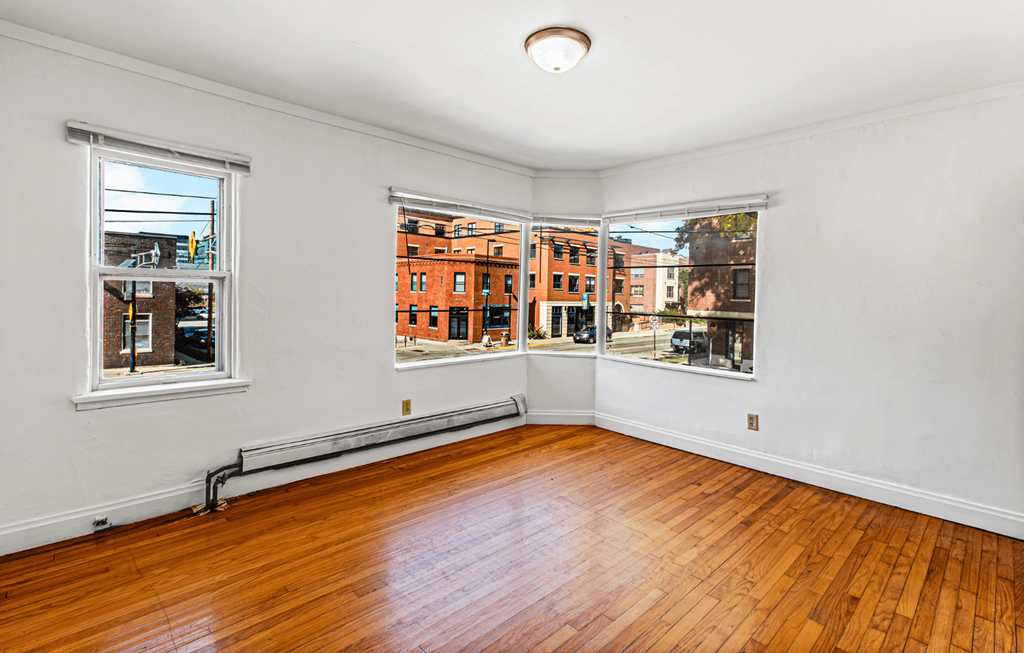 an empty living room with wood floors and three windows