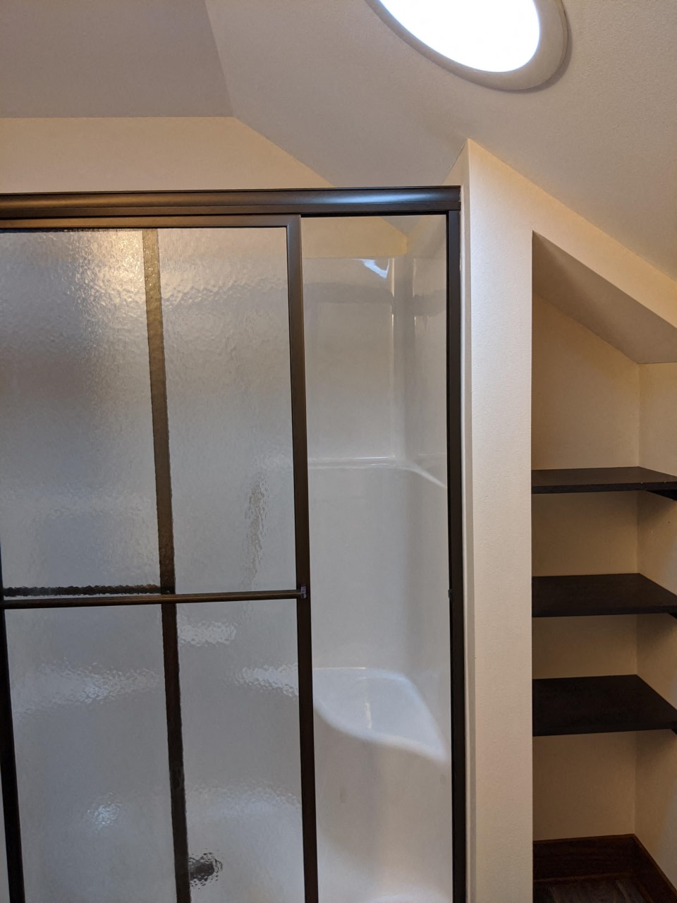 a walk in shower with a glass door and shelves