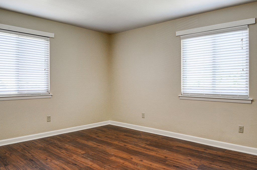 an empty room with wood floors and two windows