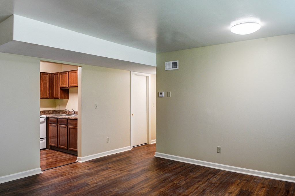 an empty living room and kitchen with wood flooring and white walls