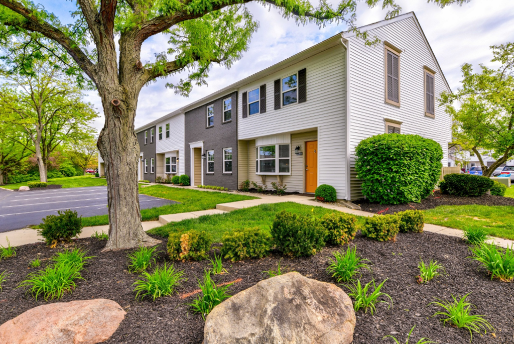a white house with a yard and trees and rocks