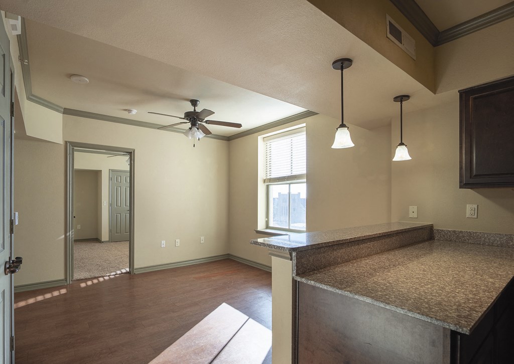 an empty living room with a kitchen and a ceiling fan