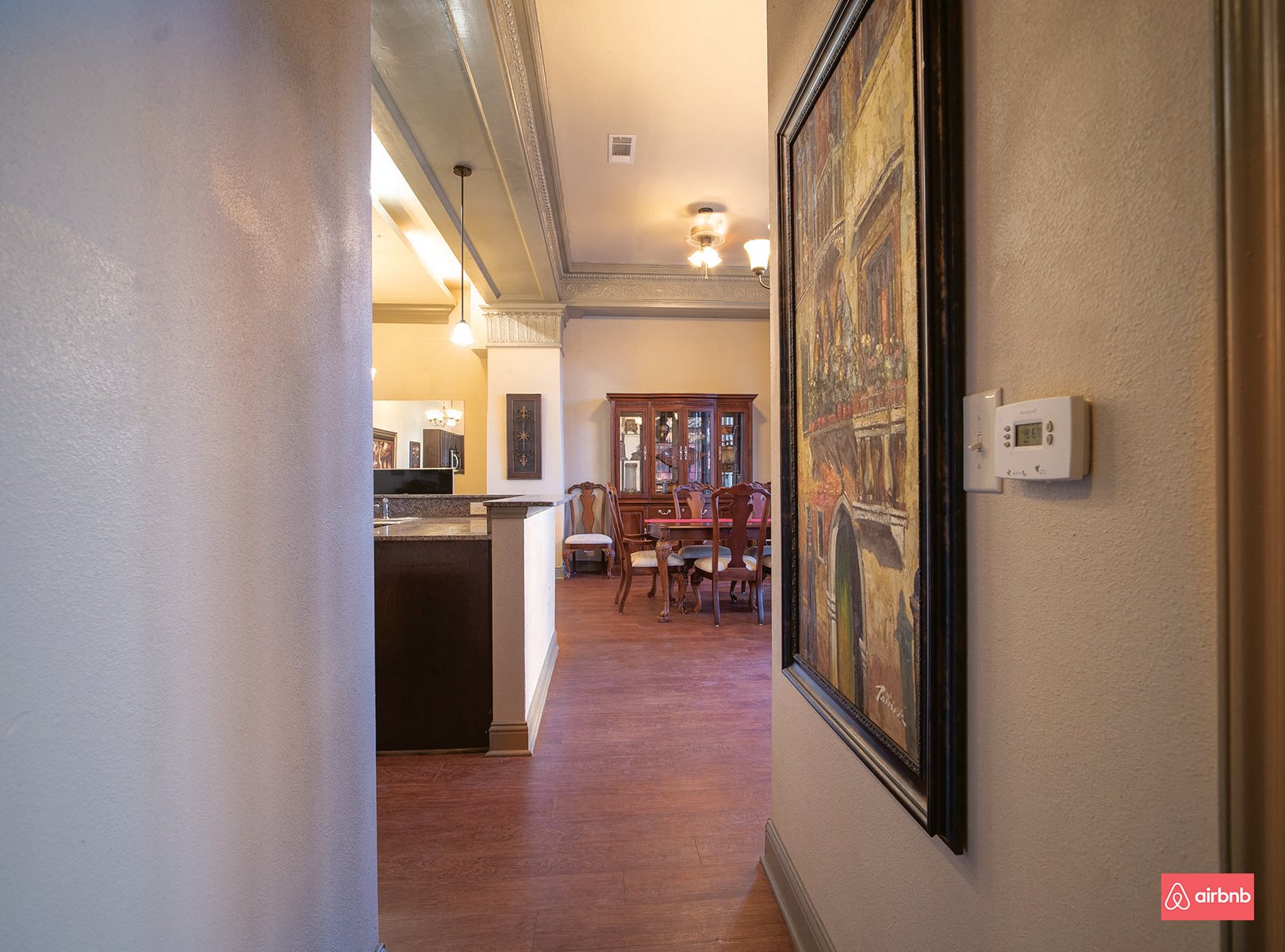 a hallway leading to a dining room and kitchen with a painting on the wall