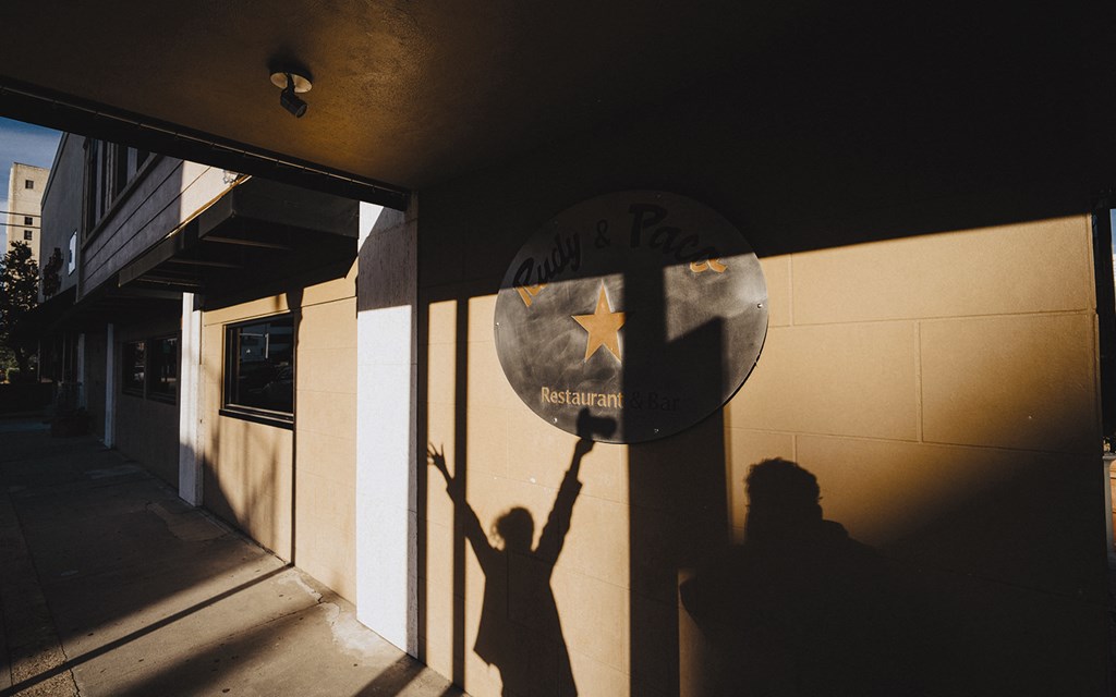 a shadow of a person holding up a street sign in front of a building