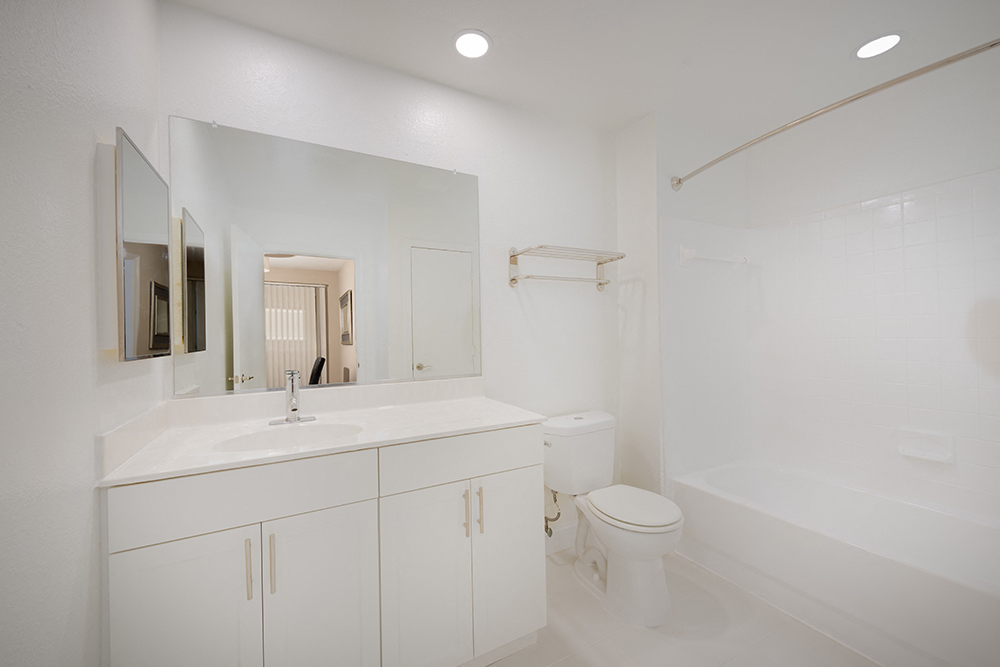 A full bathroom with tub shower, white cabinets, white ceramic tile flooring, large mirror.
