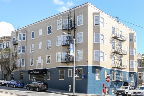 an apartment building on the corner of a street with cars parked