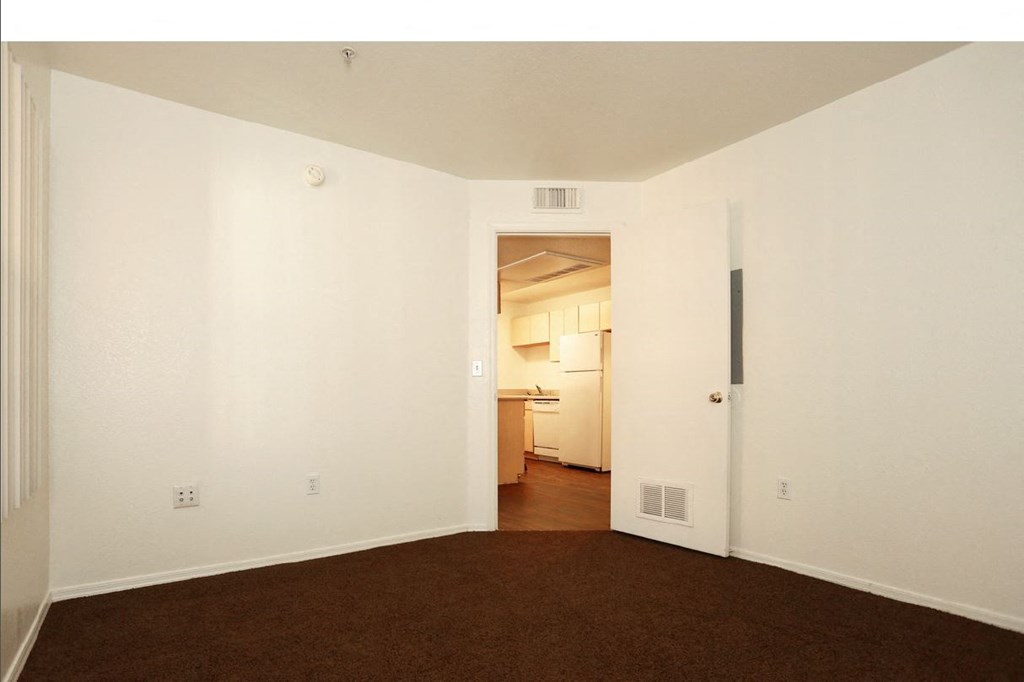 an empty living room with white walls and a door to a kitchen