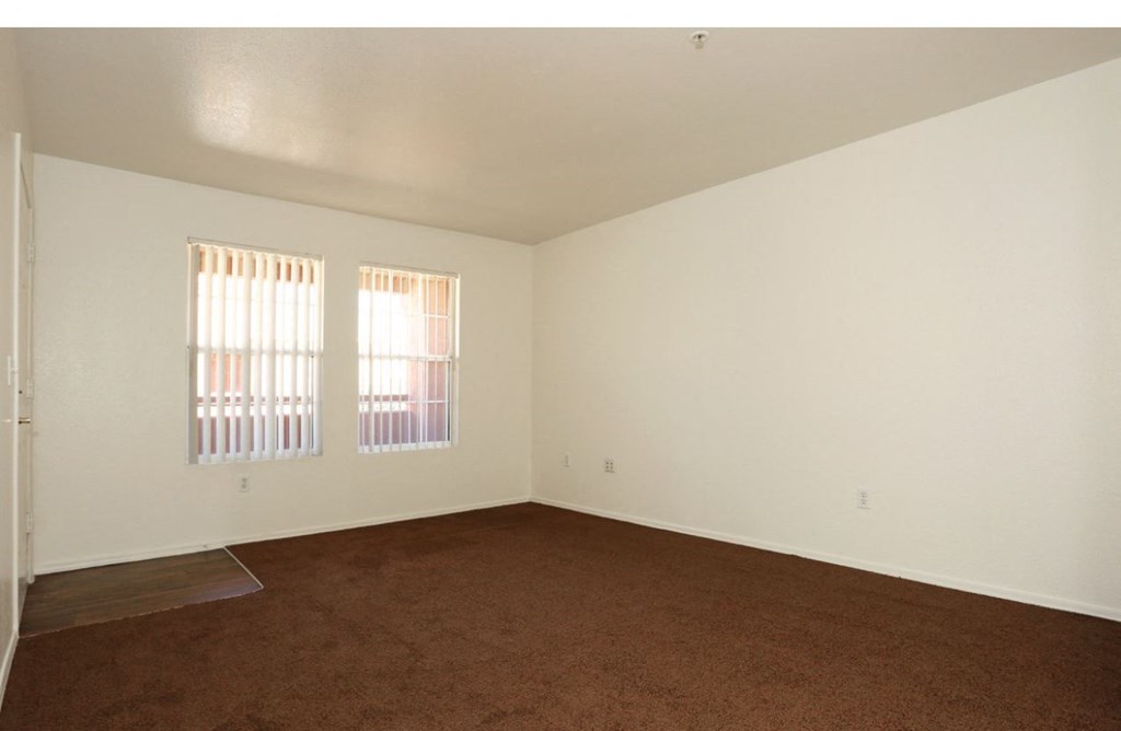 an empty living room with carpet and two windows