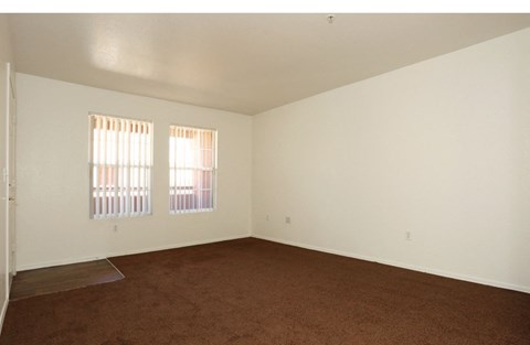 an empty living room with carpet and two windows