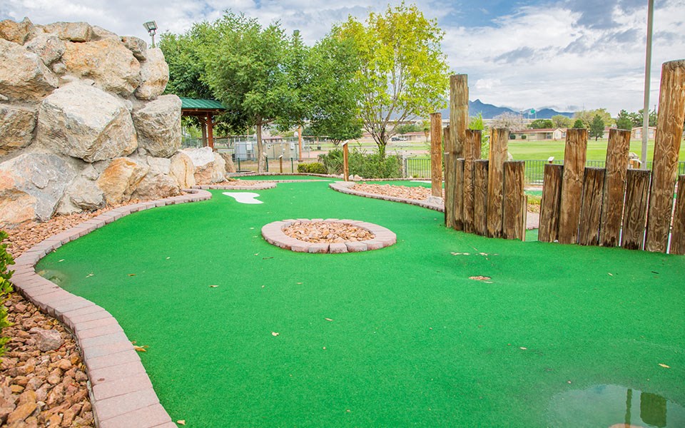 a mini golf course with a rock wall and wooden fence