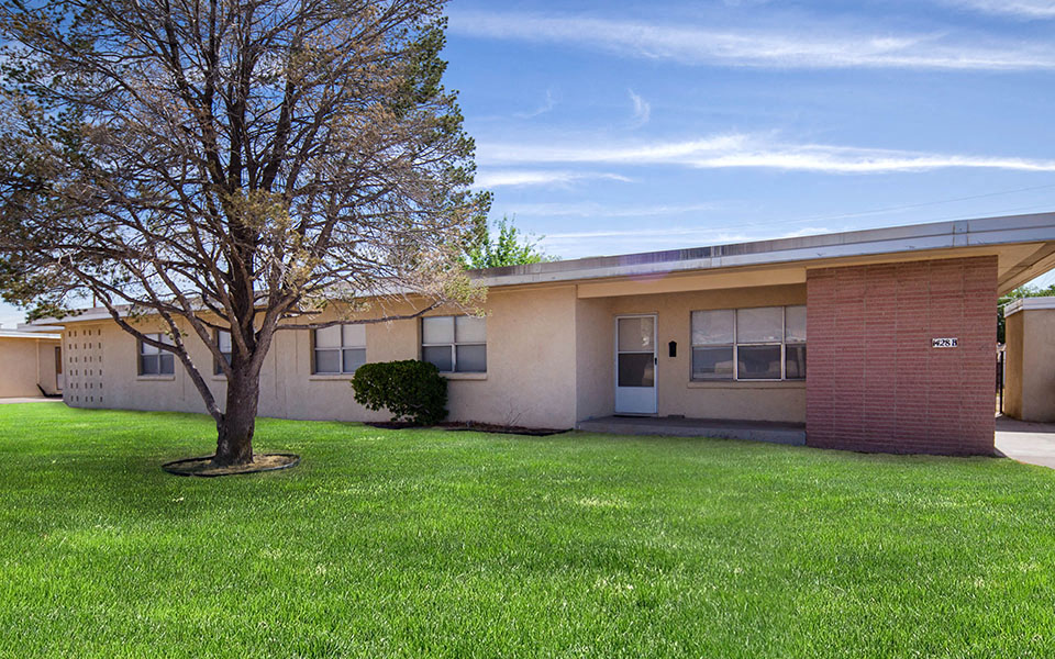 the front of a house with a grassy yard and a tree