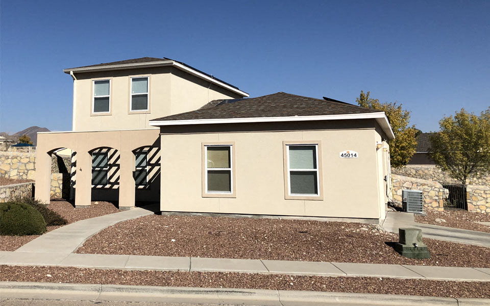 a small tan house with a sidewalk in front of it