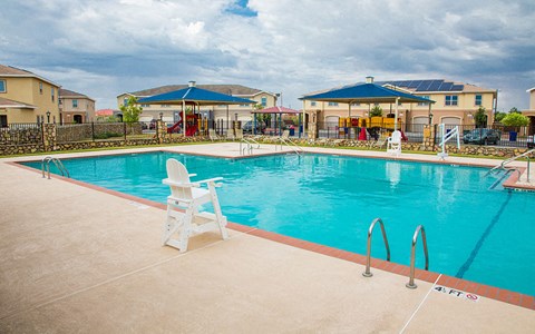 a large swimming pool with chairs and buildings in the background