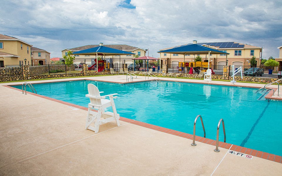 a large swimming pool with chairs and buildings in the background