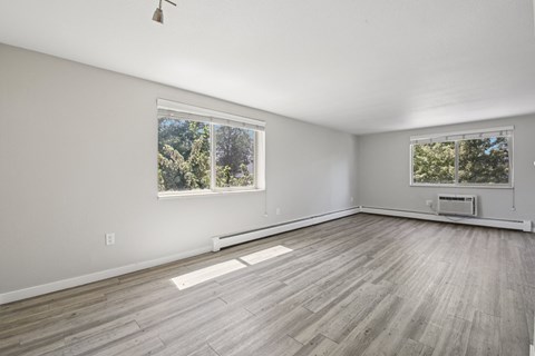 A spacious room with wooden flooring and two windows.