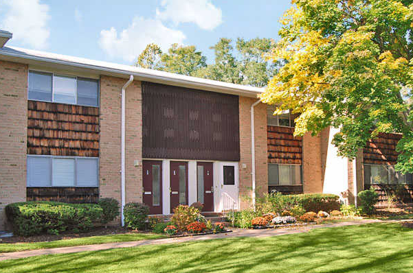 the front of a brick apartment building with a lawn and trees