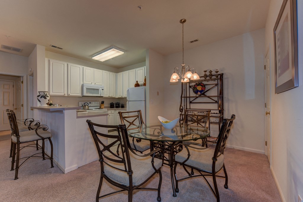 a dining area with a glass table and chairs and a kitchen