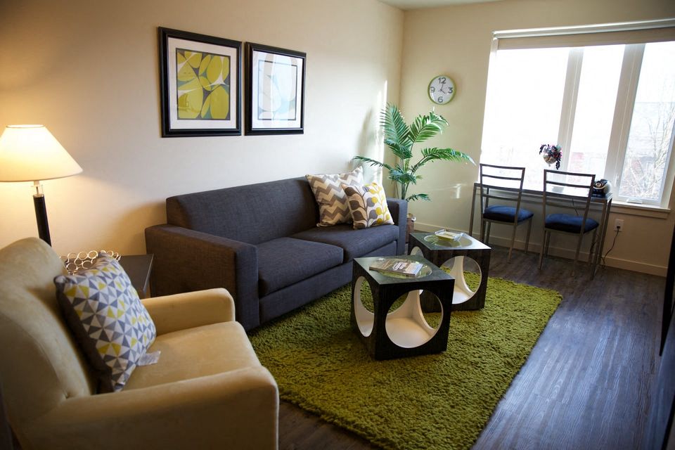 A living room with a grey couch, a yellow chair, and a green rug.