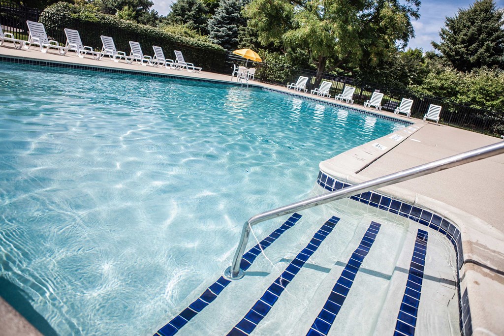 A swimming pool with blue tiles and white lounge chairs.