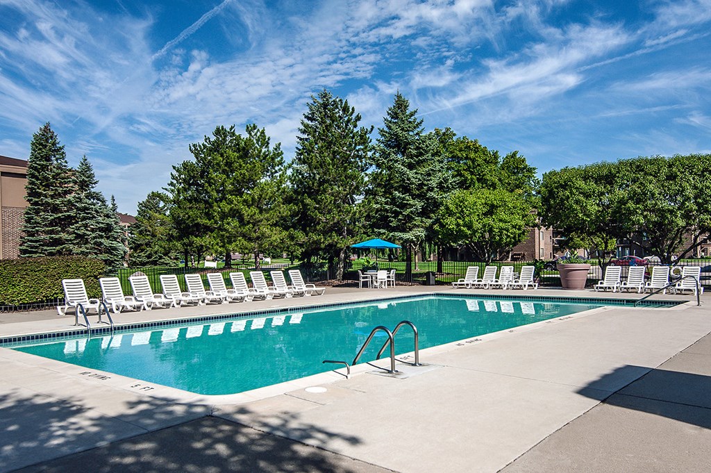 a swimming pool with white chairs around it and trees
