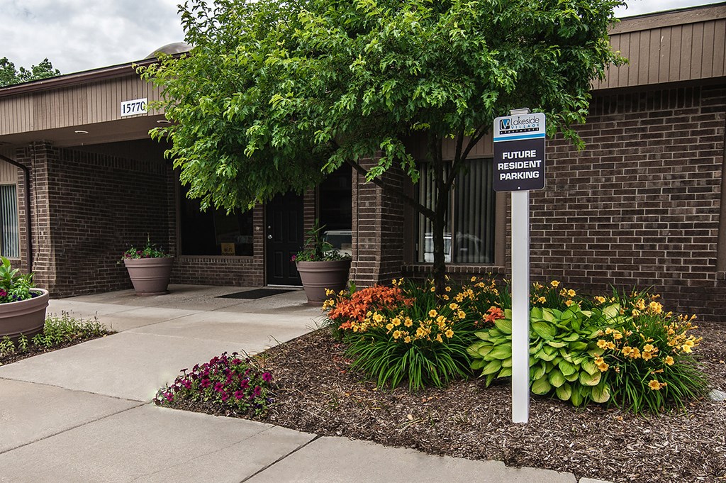 a sign in front of a building with flowers and a tree
