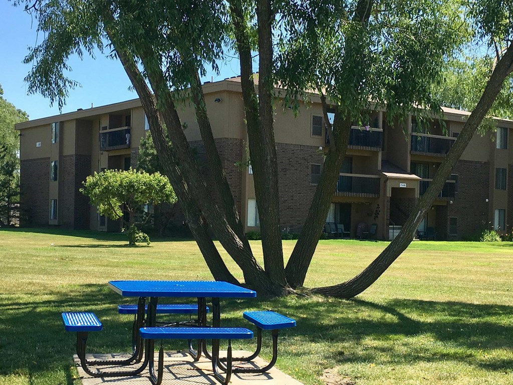 two picnic tables sitting under a tree in front of an apartment building