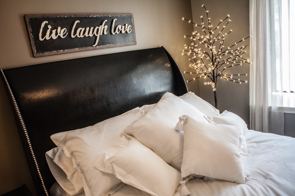 a bed with white pillows under a sign that reads live laugh love