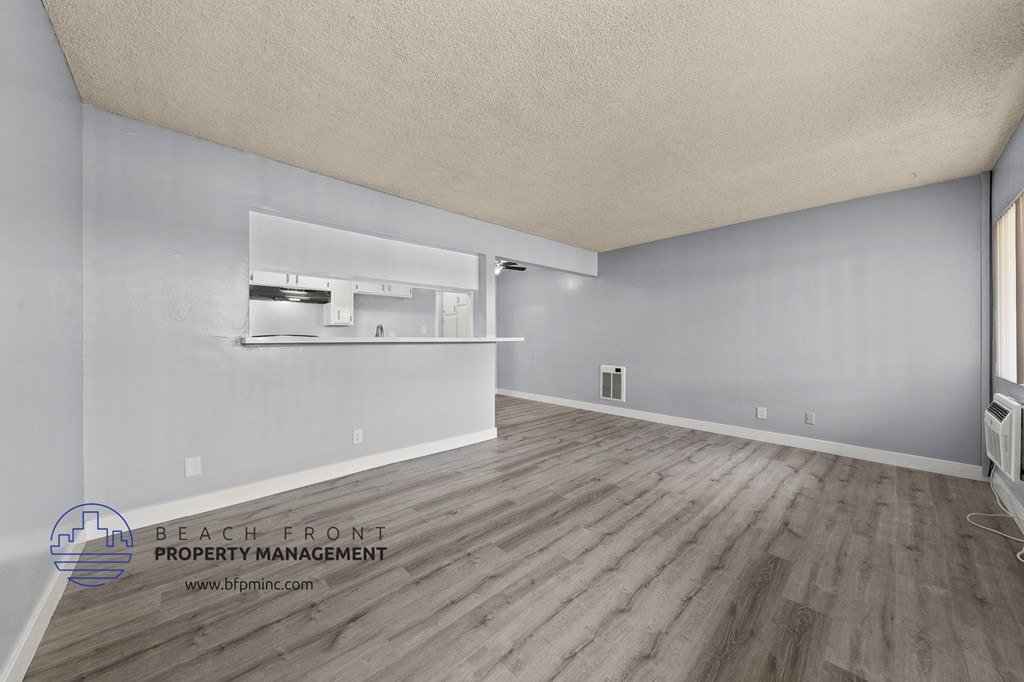 the living room and kitchen of an apartment with white walls and wood flooring