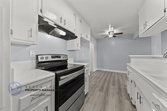 a white kitchen with white cabinets and black appliances and a ceiling fan