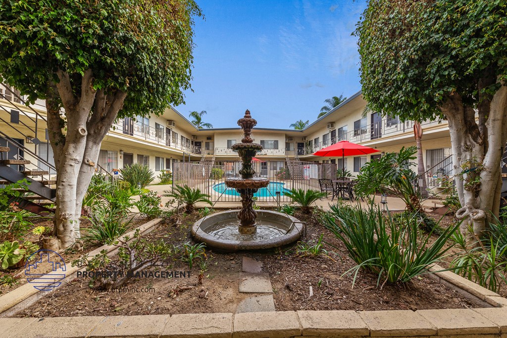 a fountain in the middle of a courtyard with trees and a pool