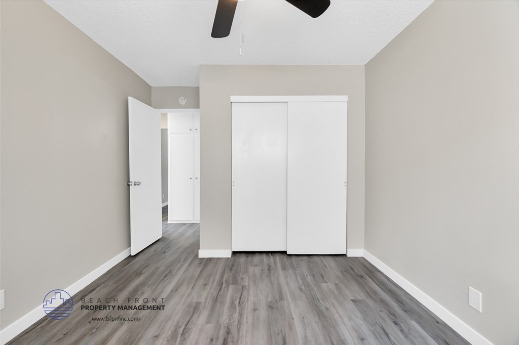 a bedroom with white walls and wood flooring and a closet