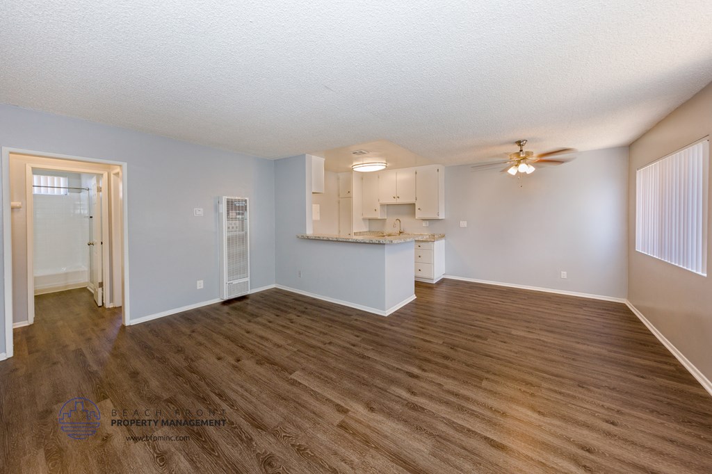 an empty living room with a kitchen and a ceiling fan